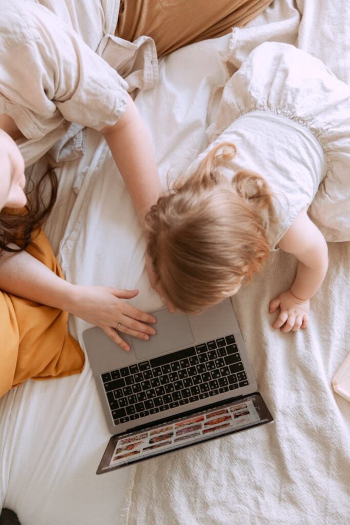 Crop mother with anonymous daughter typing on laptop in bedroom